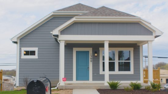 A one-story house with a door and two windows on the front. The home is painted a blueish gray and the door is a turquoise blue.