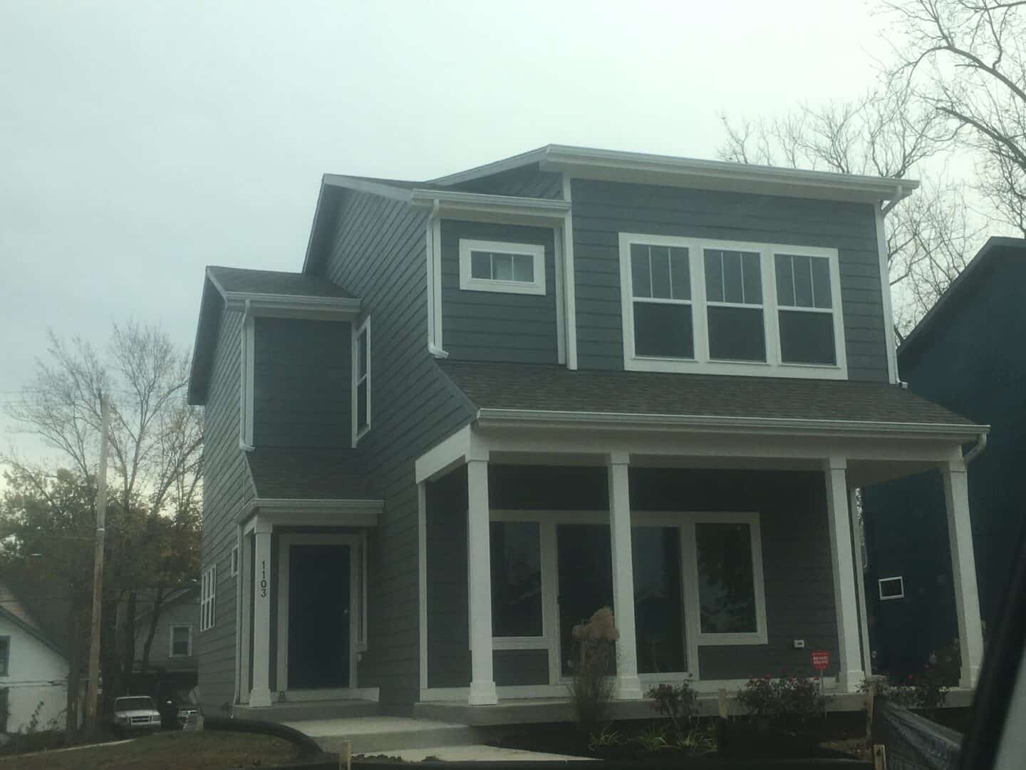 A two-story home with 3 windows visible on the upper story and a large glass door on the ground level. The front entry is to the left facing the house.