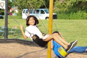 A girl is swinging on a swing outdoors. She has a big smile on her face.