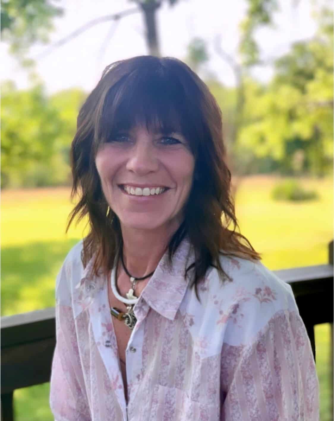 Cecelia, a woman with a bright smile and dark, shoulder-length hair is smiling against a sunny green backdrop.