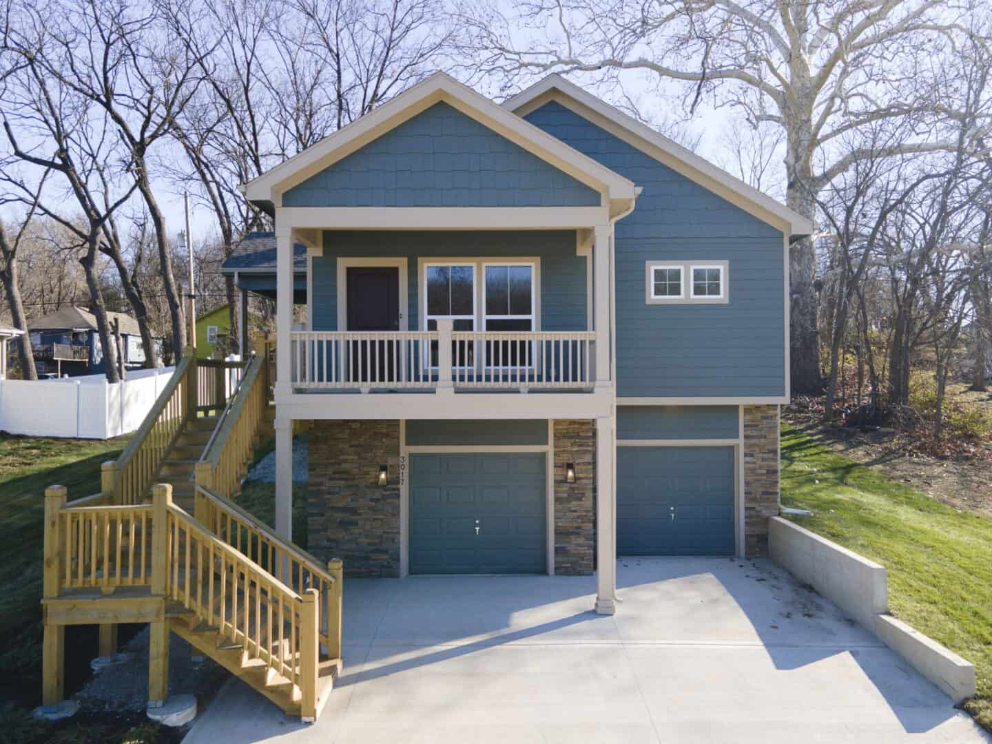 A photo of a blue two-story house with a drive-under garage, exterior front staircase, front porch, and white trim.