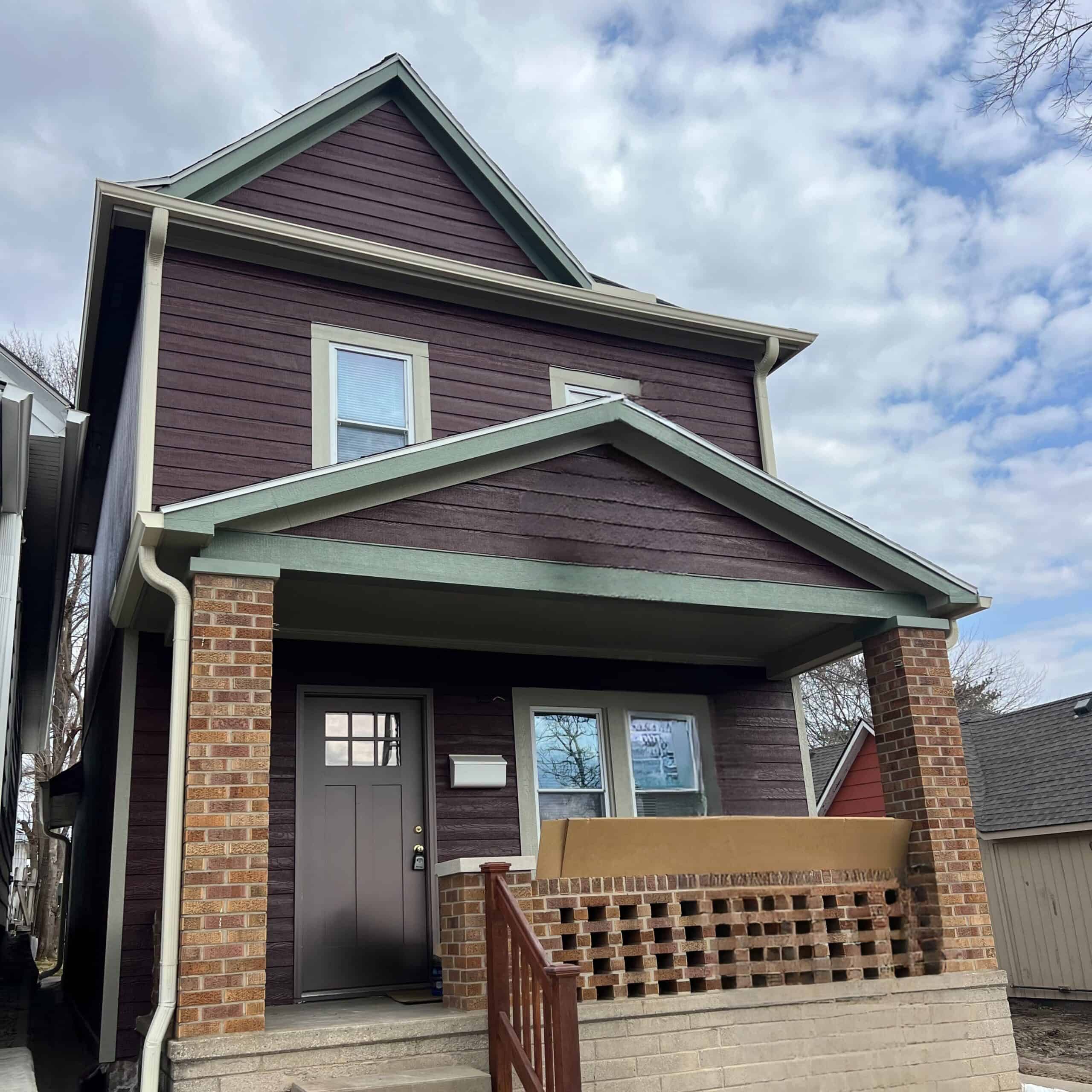 A home with at least two stories and 2 windows on each floor. There are concrete steps up to a small porch with a low brick wall.