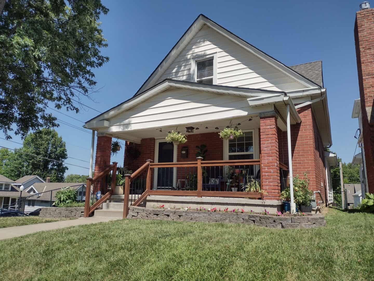 A brick home with siding on the second story. The home has a porch in the front and a garden around the side.
