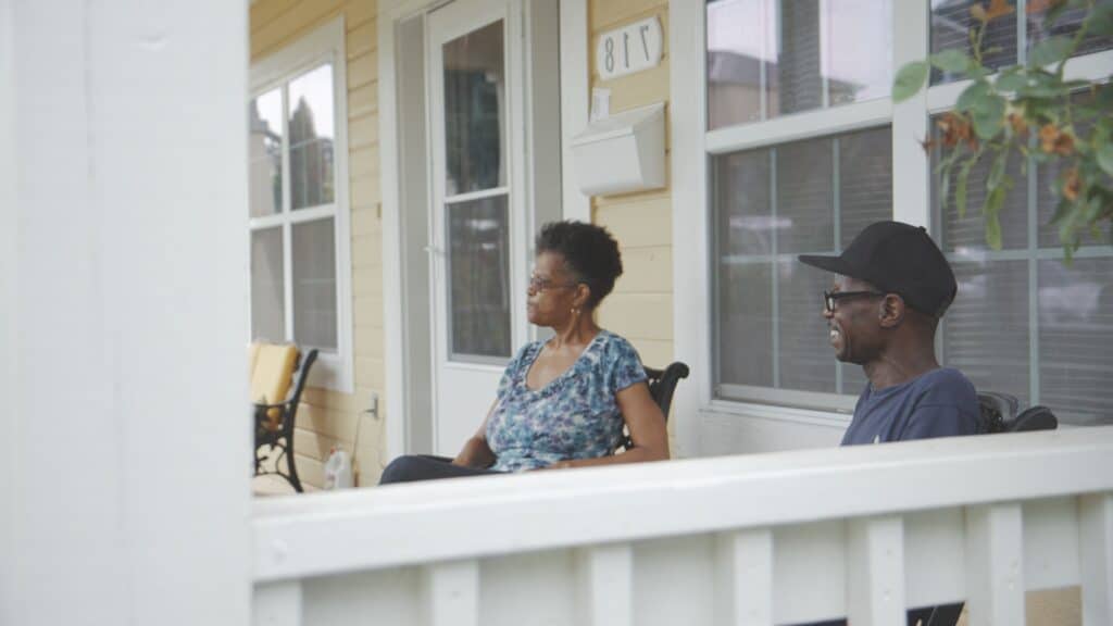 A family of two sits on their front porch in front of their beautiful home.