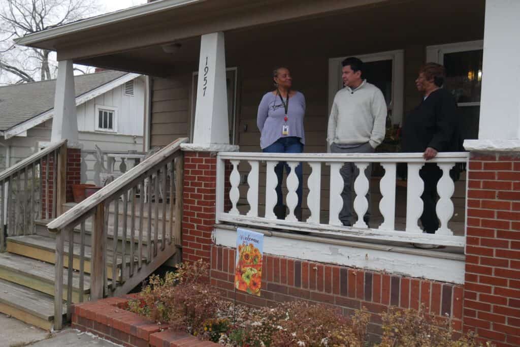 A Black woman and a Hispanic man stand on the front porch of a nice home.