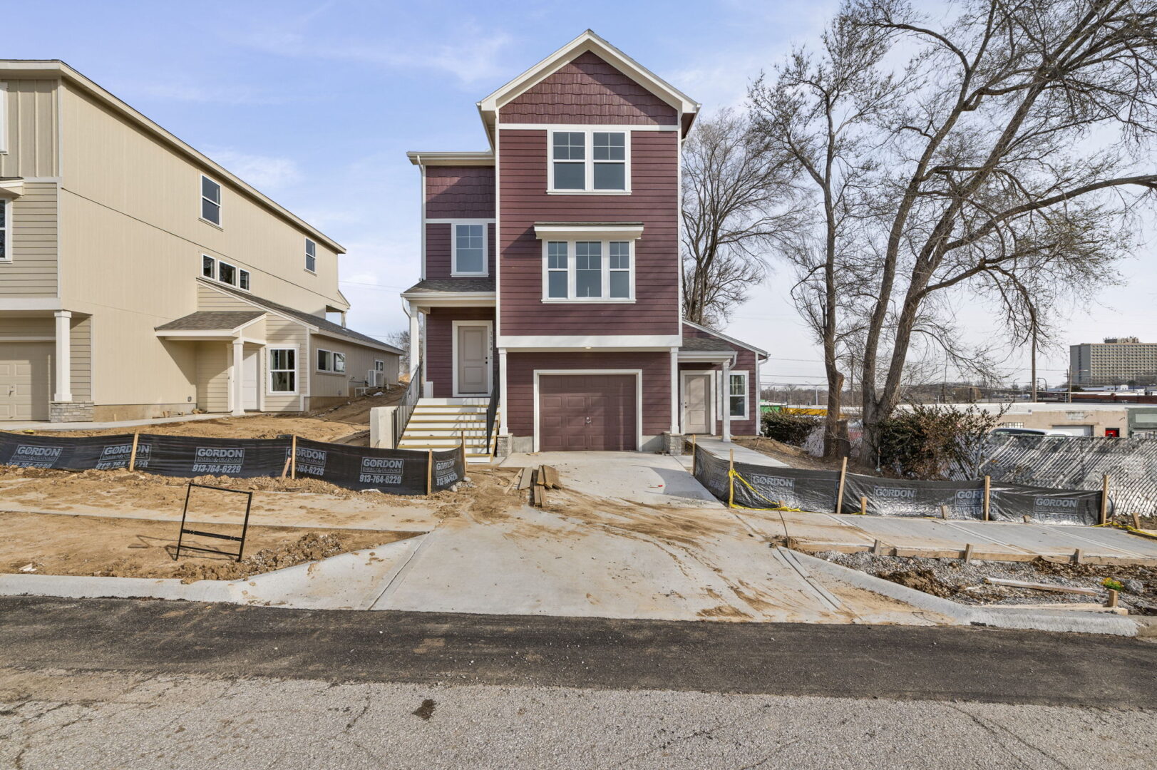 A brand new multi story home with a tuck under garage and entrances on both sides, featuring a rich red brown exterior with white paint.