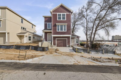 A brand new multi story home with a tuck under garage and entrances on both sides, featuring a rich red brown exterior with white paint.