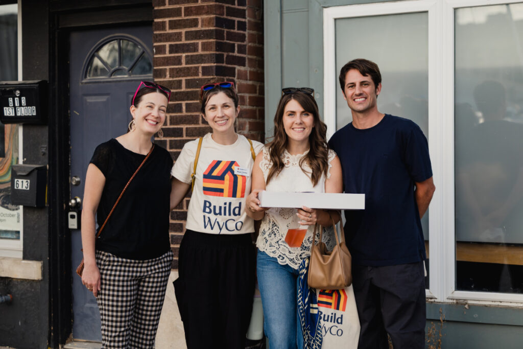 A group of people standing on a street smiling together while holding a box