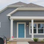 a one-story home painted purple-grey with white trim and a turquoise front door.