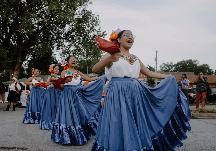 A group of girls in dresses with wide blue skirts dances in the street.